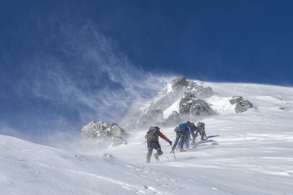 Alpinistas en grupo ascendiendo una montaña nevada con fuerte viento.