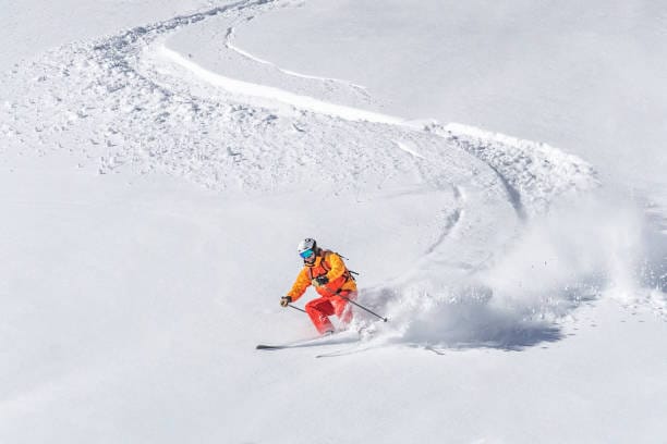 Esquiador realizando varios giros medios en nieve polvo.