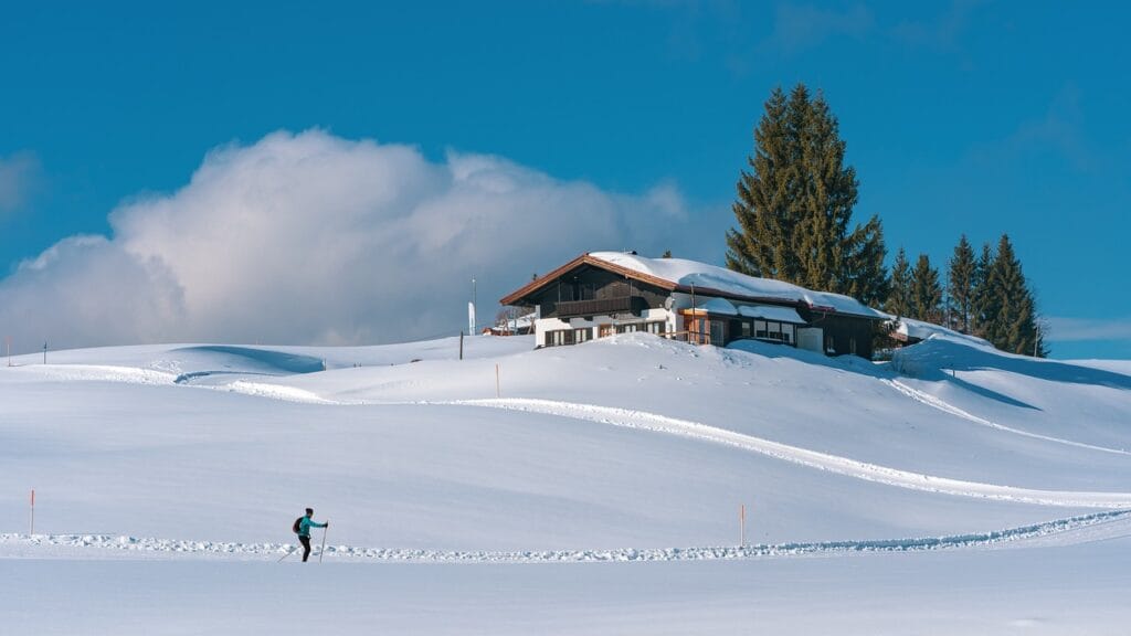 Paisaje nevado junto a un refugio por el que transcurren las pistas de esquí. Se puede apreciar a un esquiador disfrutando de la nieve.